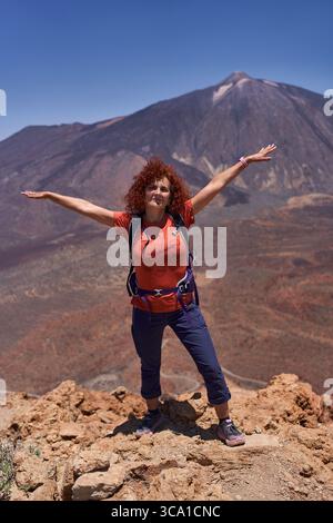 Rothaarige Wanderer, die mit ausgestreckten Armen vor dem Pico del Teide unter einem klaren blauen Himmel steht Stockfoto