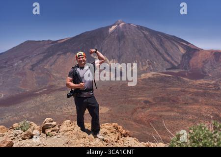 Fröhlicher Wanderer posiert mit gebeugten Armen auf einem felsigen Aussichtspunkt mit Pico del Teide im Hintergrund Stockfoto