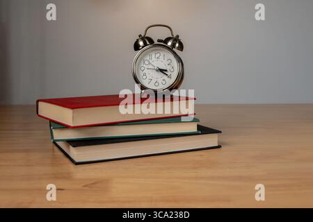 Klassischer Wecker auf Büchern mit warmer Beleuchtung in ruhiger Innenumgebung. Stockfoto