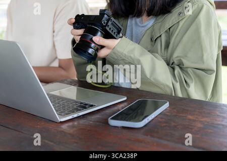 Frau prüft Fotos auf ihrer Digitalkamera mit einem Laptop an ihrer Seite, arbeitet oder bearbeitet Bilder. Stockfoto