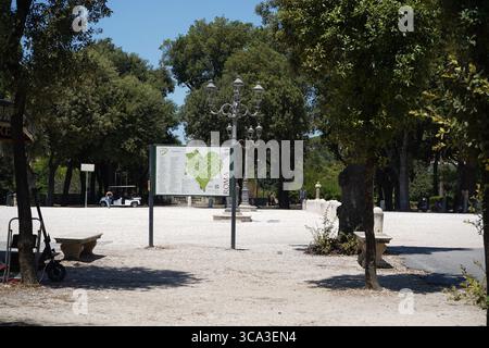 Villa Borghese Park an einem sonnigen Sommertag. Ein großes Informationsschild steht in einem ruhigen, von Bäumen gesäumten, offenen Bereich, ideal für Tourismus und Aktivitäten. Stockfoto