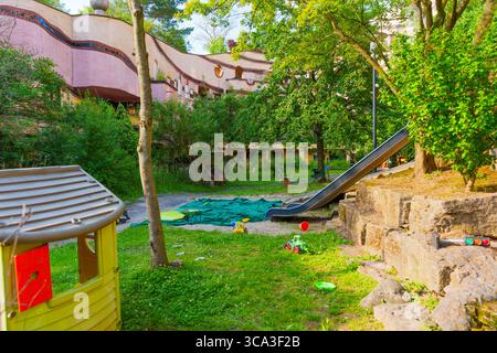 Lebendiger Spielbereich mit Rutsche und Kinderspielzeug inmitten üppiger Grünanlagen in der Waldspirale, einem architektonisch einzigartigen Wohnkomplex in Darmstad Stockfoto