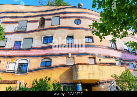Farbenfrohe Fassade des Wohnkomplexes Waldspirale mit gewellten Mustern, einzigartigen Fenstern und lebendigen Wandgemälden vor einem klaren blauen Himmel. Stockfoto