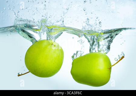 Dynamischer Spritzer frischer grüner Äpfel in klares Wasser und erzeugen lebendige Blasen und Tropfen in einer energiegeladenen und erfrischenden Szene. Stockfoto