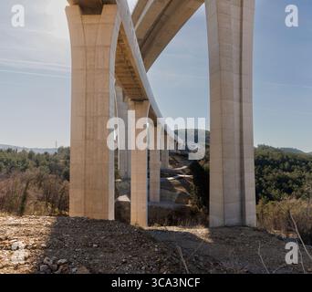 Baustelle eines Betonfertigteilbahnviadukts in einer hügeligen Landschaft. Massive industrielle Überführungen werden mit Kränen und Hea montiert Stockfoto