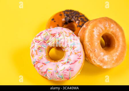 Drei verschiedene Donuts auf gelbem Hintergrund. Nahaufnahme mit selektivem Fokus. Stockfoto