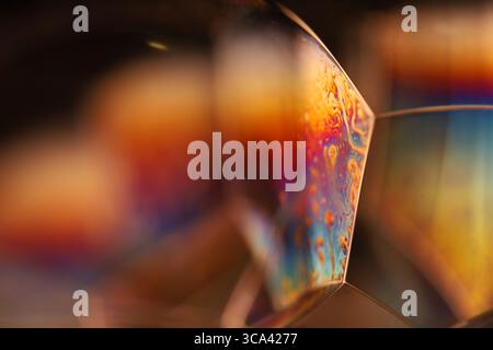 Makro aus goldenen und orangefarbenen Seifenblasenverbindungen mit schillernden Regenbogenmustern und geometrischer Strömungsbewegung Stockfoto