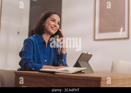 Eine junge Frau führt aktiv ein Telefongespräch in ihrem gemütlichen Heimbüro Stockfoto