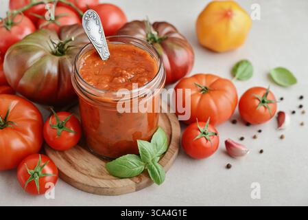 Traditionelle Tomatensauce in einem Glas mit frischem Basilikum, Reifen Tomaten, Knoblauch und Pfeffer auf hölzernem Schneidebrett, Nahaufnahme Stockfoto