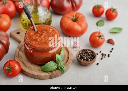 Traditionelle Tomatensauce in einem Glas mit frischem Basilikum, Reifen Tomaten, Knoblauch und Pfeffer auf hölzernem Schneidebrett, Nahaufnahme Stockfoto