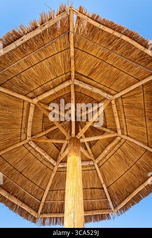 Blick auf den Strohschirm von unten (Tiki-Hüttenschirm, Strohschirm) aus getrockneten Palmblättern vor blauem Himmel an einem Strand in den Vereinigten Arabischen Emiraten. Stockfoto