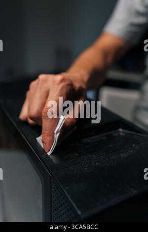 Vertikale Nahaufnahme der Hand des Technikers, die Staub und Schmutz von der Computerhülle mit einem Tuch entfernt, um optimale Leistung und Hygiene zu gewährleisten. Stockfoto