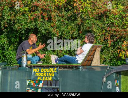 Ein Mann und eine Frau, die auf einem Schmalboot sitzen und plaudern, auf dem Lea Valley Kanal, Lee Navigation, Tottenham, London, England. Alternative Wohnen in London. Stockfoto