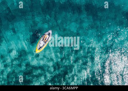 Frau mit Strohhut, die sich in einem aufblasbaren Kajak auf der türkisfarbenen Adria entspannt, Blick von oben. Sommerurlaub, Küstenreisen, exotisches Reiseziel, Ruhe Stockfoto