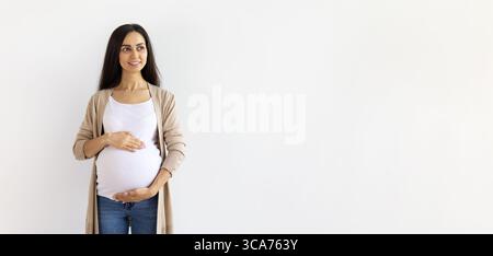 Glückliche junge schwangere Frau in lässigen Kleidern, die den Bauch berührt und lächelt Stockfoto