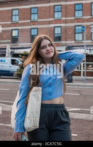 Eine junge Frau in blauem Crop-Top und grauer Jogginghose steht an einem Ziegelgebäude Stockfoto