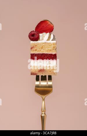 Der bento-Kuchen mit Vanilleschwamm besteht aus Himbeeren und Erdbeeren, elegant garniert mit Schlagsahne und frischem Obst, gehalten von einer goldenen Gabel Agave Stockfoto