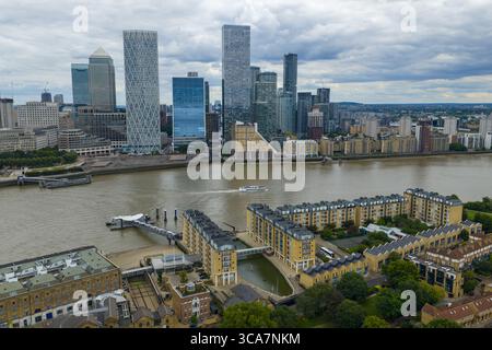 Luftbild mit den Türmen der Canary Wharf hinter Wohngebäuden am Fluss und dem Anlegesteg. Stockfoto