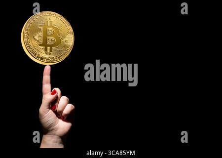 Idee und Erfolgskonzept. Goldener Bitcoin auf weiblicher Hand mit Abzugsfinger und roten Nägeln auf schwarzem Hintergrund. Kopierbereich Stockfoto