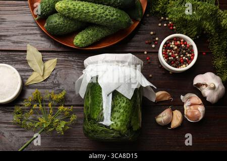 Eingelegte Gurken im Gefäß, frische Gurken, Knoblauch, Dill und Gewürze auf Holztisch, flach gelegt Stockfoto