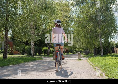 An einem hellen, sonnigen Tag fährt eine Person mit dem Fahrrad einen Kiesweg entlang, der von üppigen Bäumen und Grün umgeben ist. Stockfoto