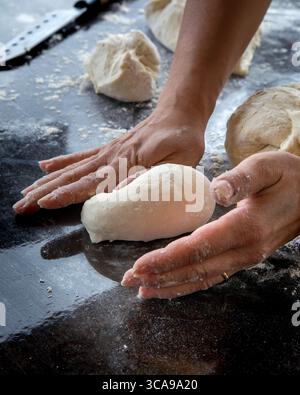 Nahaufnahme einer Hand, die frischen Teig auf einer bemehlten Arbeitsplatte kneten. Hausgemachter Backprozess in einer warmen und rustikalen Küchenumgebung. Stockfoto