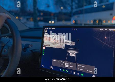 Weibliche Fahrerin im Tesla Model Y Elektroauto mit Autopilot und seitlicher Kameraansicht auf der Winterstraße. Schweden. Uppsala. Stockfoto