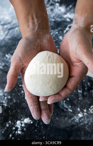 Eine Nahaufnahme einer Person, die sanft eine frisch geformte Teigkugel in ihren bemehlten Händen hält. Stockfoto