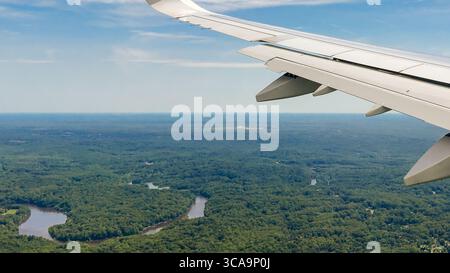Weitläufige Ackerflächen, Wälder und Vorstädte erstrecken sich über die Landschaft, von einem Flugzeugfenster aus gesehen. Stockfoto