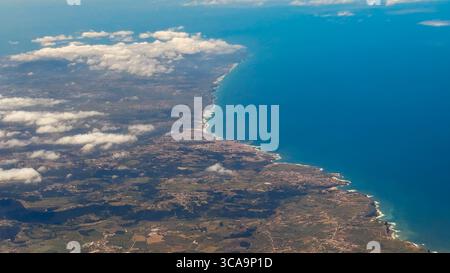 Die zerklüftete Küste trifft auf das tiefblaue Meer, während verstreute Wolken über Dörfern und Ackerland im Landesinneren schweben. Stockfoto