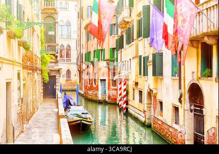 Wunderschöner schmaler Kanal und Straße mit Booten, europäische union, venedig und italienische Flaggen in Venedig während des Sommertages, Italien Stockfoto