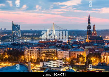 Wunderschönes Panorama von Riga Zentrum und Vansu Brücke über den Daugava Fluss während des atemberaubenden Sonnenuntergangs. Blick auf die beleuchtete Stadt Riga, die Hauptstadt von Lettland Stockfoto