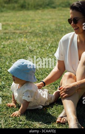 Eine Mutter genießt einen sonnigen Sommertag im Freien mit ihrem Baby. Die freimütige Szene fängt Wärme, Verbundenheit und die Freude ein, Zeit zusammen in der Natur zu verbringen. Stockfoto
