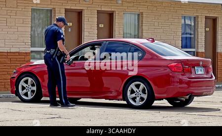 11. Mai 2023, Emporia, Kansas, USA: Der Polizeibeamte der Stadt Emporia erklärt dem Fahrer des roten BMW, warum er einen Verkehrsstopp durchführt. Der Offizier hält seine Radarkamera in der rechten Hand und zeigt sie dem Fahrer, damit der Fahrer sehen kann, wie schnell er fuhr. (Bild: © Mark Reinstein/ZUMA Press Wire) Stockfoto