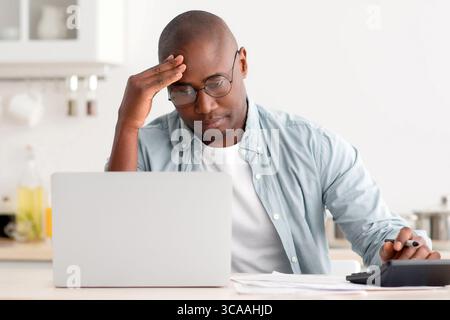 Gestresst reifen schwarzen Mann mit Rechner und Laptop-Computer, Berechnung der Steuern, Überprüfung der monatlichen Ausgaben Stockfoto