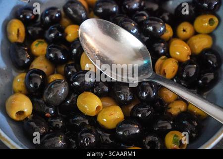 Gemischte Oliven, serviert in einer Schüssel mit Löffel zum Vorspeisen oder Garnieren vom Buffet. Stockfoto