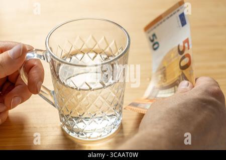 Ein Glas Wasser und eine 50-Euro-Rechnung in der Hand. Wirtschaftliches Konzept. Steigende Wasserpreise. Süßwasserprobleme in Europa. Nahaufnahme Stockfoto