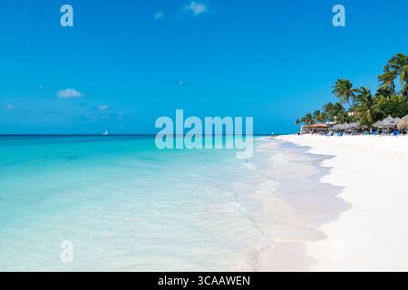 Divi Beach, Aruba: Türkisfarbenes Wasser und weicher Sand erstrecken sich zu weit entfernten Resorts unter einem lebendigen karibischen Himmel. Stockfoto