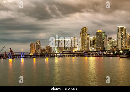 Ein atemberaubender Blick auf die Skyline der Innenstadt von Miami, mit modernen Hochhäusern, die die pulsierenden Abendlichter vor dem Abendhimmel reflektieren. Stockfoto
