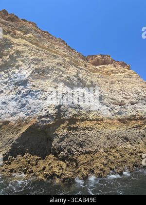 Aus nächster Nähe sehen Sie steile Kalksteinklippen an der Algarve, Portugal, mit geschichteten Felsformationen und Anzeichen von Küstenerosion unter einem klaren Himmel Stockfoto