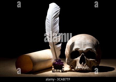 Theater- oder Theaterkonzept. Altes Tintenständer mit Feder in der Nähe der Rolle mit Schädel vor schwarzem Hintergrund. Dramatisches Licht. Stockfoto