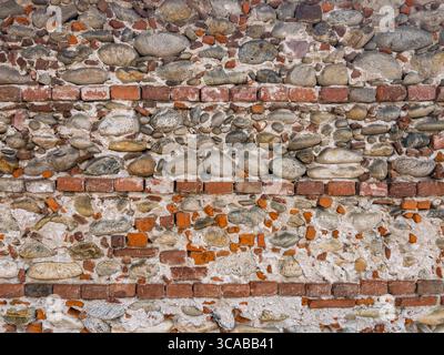Alte Mauer aus ordentlichen Reihen von alten Ziegeln gemischt mit Natursteinen, gebrochenen Ziegeln und Putz. Grafikelement für Hintergrund und Textur. Stockfoto