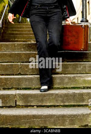 Eine Person läuft eine Steintreppe hinunter, während sie einen braunen Koffer trägt. Stockfoto