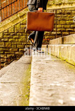 Eine Person in Anzug und Fersen geht eine Steintreppe hinauf, während sie eine Aktentasche trägt. Stockfoto