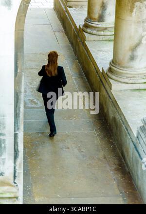 Eine Frau in einem schwarzen Anzug läuft einen Steingang hinunter. Stockfoto