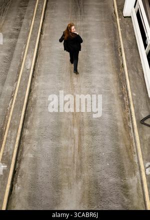 Eine Frau in einem schwarzen Anzug läuft einen konkreten Weg. Stockfoto