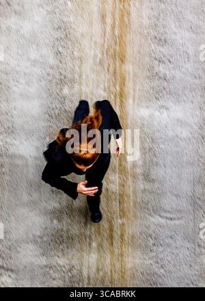 Eine Frau mit rotem Haar läuft auf einer strukturierten Oberfläche, möglicherweise einer Wand oder einem Wasserfall, von oben gesehen. Stockfoto