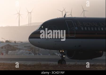 Larnaca, Zypern - 29. Juni 2024: Das jordanische Flugzeug fährt bei Sonnenuntergang auf der Landebahn, Windräder und Flughafengebäude im Hintergrund Stockfoto