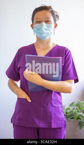 Ärztin mit violetten Peelings und chirurgischer Maske, die während der covid-19-Pandemie in einem Krankenhauskorridor eine Patientenakte hält Stockfoto