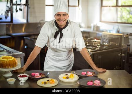 Männlicher Koch in Kochjacke hinter der Theke, der Kuchen Macarons Himbeeren in der Küche präsentiert Stockfoto